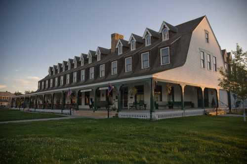 A large, historic hotel with a white exterior and multiple gabled roofs, surrounded by green grass and a clear sky.