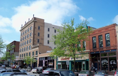 A vibrant downtown scene featuring historic buildings, shops, and trees under a clear blue sky.