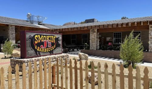 A rustic barbecue restaurant with a colorful sign reading "Smokin' J's Barbecue" and a fenced outdoor area.