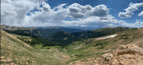 A panoramic view of lush green mountains under a blue sky with fluffy clouds, showcasing a serene natural landscape.