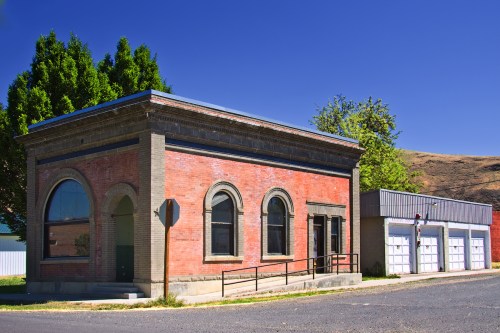 Historic brick building with arched windows, next to a modern garage, set against a clear blue sky.