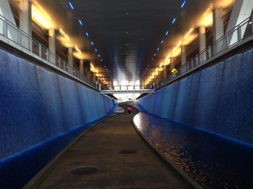 A serene, illuminated corridor with blue water features on both sides, leading to a bright exit.
