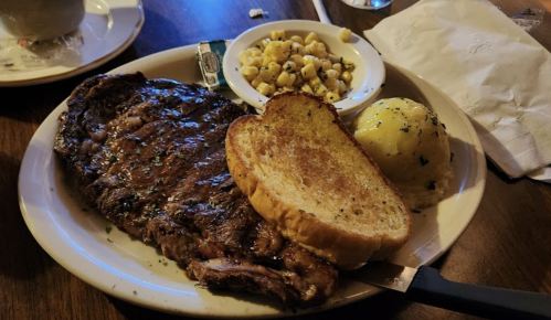 A plate featuring a grilled steak, garlic bread, a baked potato, and a side of corn.