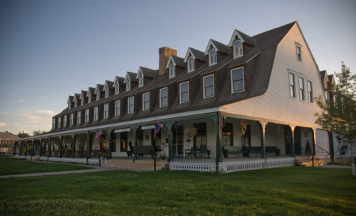 Historic multi-story hotel with a gabled roof, surrounded by green grass and a clear sky at sunset.