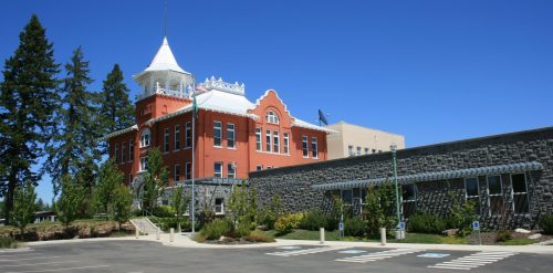 Historic red brick building with a white tower, surrounded by trees and a clear blue sky.