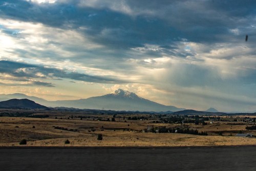 A scenic view of a mountain under a cloudy sky, with rolling hills and fields in the foreground.