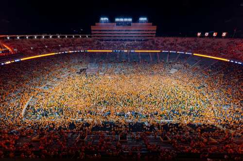 A packed stadium at night filled with fans wearing orange, celebrating an event on the field.