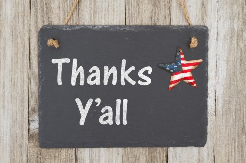 A slate sign with the text "Thanks Y'all" and a decorative star in red, white, and blue on a wooden background.