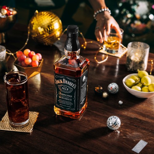A bottle of Jack Daniel's whiskey on a table with drinks, snacks, and festive decorations in a lively setting.