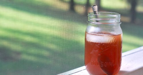 A mason jar filled with iced tea sits on a windowsill, with green trees blurred in the background.