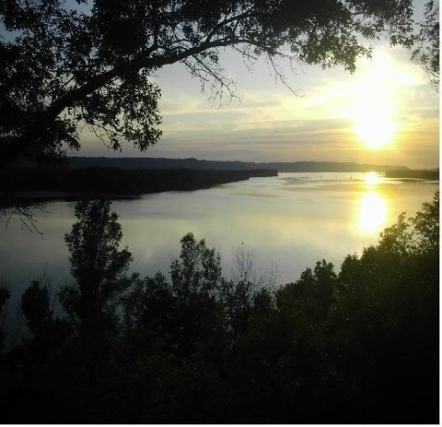 A serene river scene at sunset, with trees framing the view and soft light reflecting on the water.