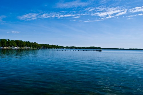 A serene lake scene with a wooden pier extending into calm blue waters under a clear sky.