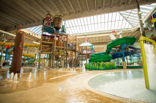 Indoor water park featuring colorful slides, play structures, and a splash area with fountains. Bright and spacious atmosphere.