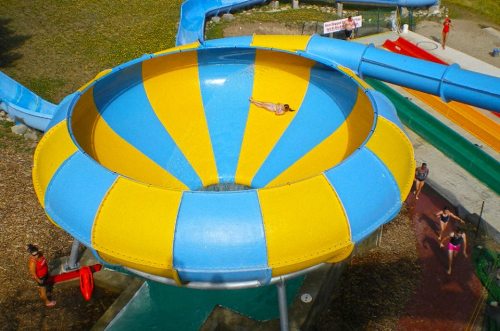 Aerial view of a colorful water slide with a person sliding down and others enjoying the water park.