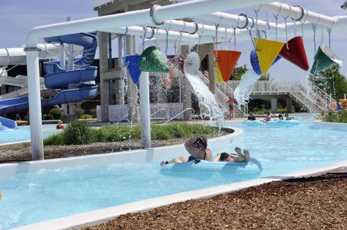 A water park scene with colorful water slides, splash features, and people enjoying the lazy river on inner tubes.
