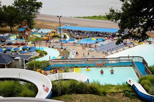Aerial view of a water park with slides, pools, and sunbathing areas, surrounded by greenery and a road in the background.