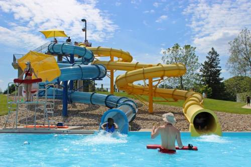 A water park scene featuring colorful slides, a lifeguard tower, and people enjoying the pool on a sunny day.