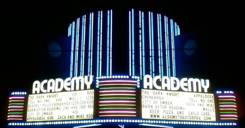 Neon-lit marquee of the Academy theater displaying movie titles and showtimes, including "The Dark Knight" and "City of Ember."