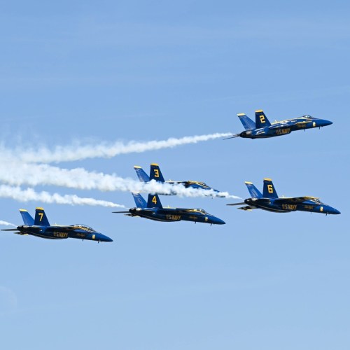 Five blue and yellow fighter jets flying in formation, leaving trails of smoke against a clear blue sky.