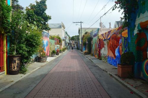 A colorful alleyway lined with vibrant murals and greenery, leading to a distant figure walking down the path.