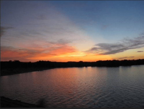 A serene sunset over a calm lake, with vibrant orange and purple hues reflecting on the water's surface.