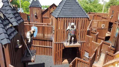 A wooden maze with castle-like structures, featuring knights on platforms and shields, set in a sunny outdoor area.