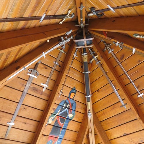 A wooden ceiling with various swords mounted, featuring a painted knight on the wall.