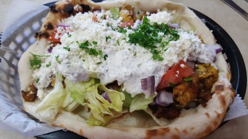 A plate of flatbread topped with grilled meat, lettuce, tomatoes, onions, and a generous sprinkle of cheese and sauce.