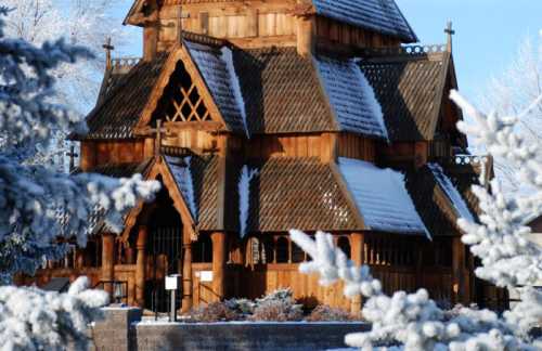 A wooden church with intricate architecture, surrounded by snow-covered trees on a clear winter day.