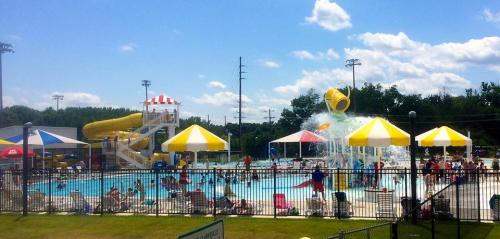 A vibrant water park scene with a pool, water slide, and colorful umbrellas, filled with people enjoying the sun.