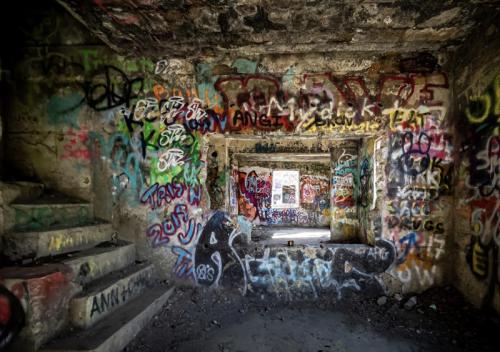 Graffiti-covered walls inside an abandoned building, with visible doorways and stairs leading to different areas.