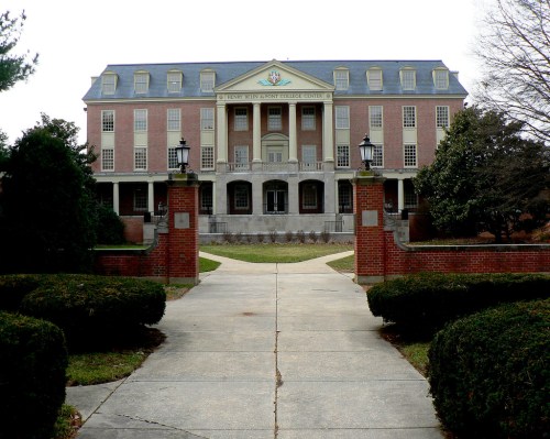 A large brick building with a grand entrance, flanked by trees and a pathway leading to it.