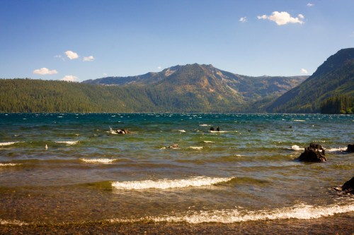 A serene lake surrounded by mountains, with gentle waves and a clear blue sky dotted with clouds.