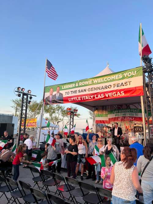 Crowd enjoying the San Gennaro Feast in Little Italy, Las Vegas, with flags and a stage in the background.
