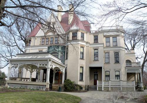 A large, historic mansion with intricate architecture, featuring a wraparound porch and multiple gables.