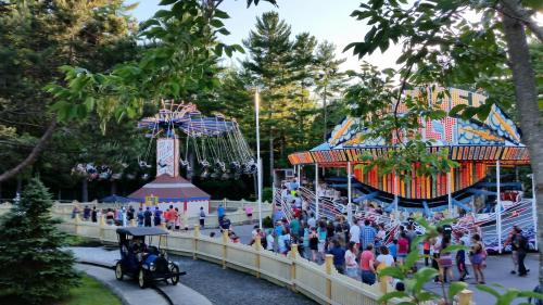A vibrant amusement park scene with a swing ride and carousel, filled with people enjoying a sunny day.