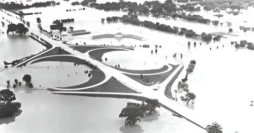 Aerial view of a flooded area, showing submerged roads and trees, with water covering the landscape.
