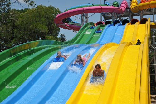 People sliding down colorful water slides, splashing into a pool below on a sunny day.