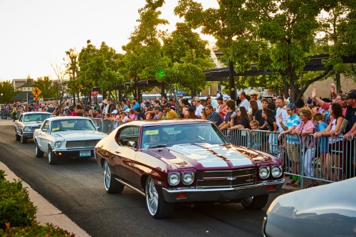 A classic car parade with a crowd of spectators lining the street, enjoying the vintage vehicles.