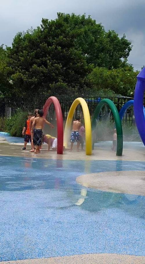 Children playing in a splash pad with colorful arches, enjoying water sprays on a sunny day.