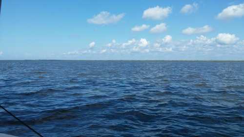 A serene view of calm blue waters under a clear sky with scattered clouds.