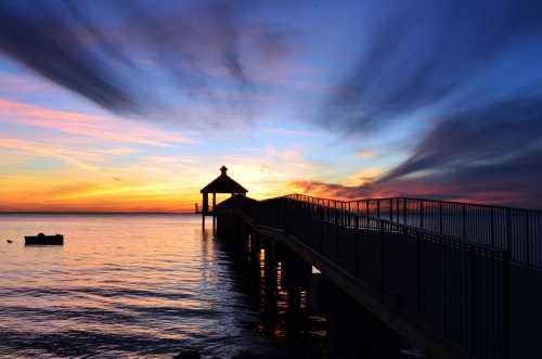 Silhouette of a pier at sunset, with vibrant clouds reflecting on calm water.