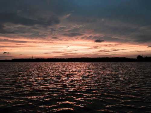 A serene sunset over a calm body of water, with dark clouds and vibrant colors reflecting on the surface.