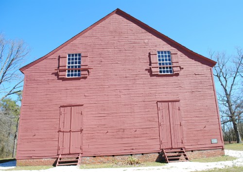 A large red barn with two sets of doors and windows, set against a clear blue sky and bare trees.