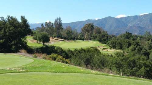 A scenic view of a golf course with rolling hills and mountains in the background under a clear blue sky.