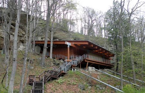 A modern wooden building nestled among trees on a hillside, with stairs leading up to it.