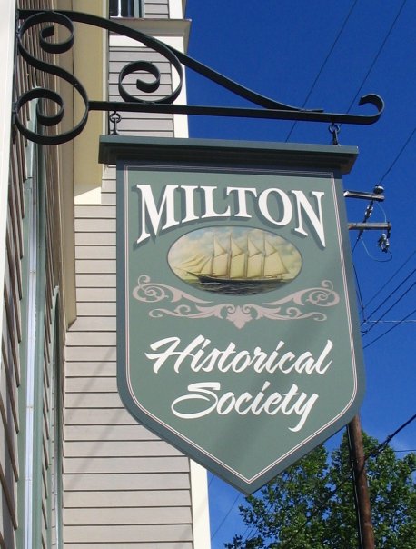 Sign for the Milton Historical Society featuring a ship illustration against a blue sky.