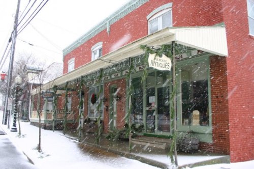 A charming antique shop covered in snow, with festive decorations and a cozy atmosphere on a winter day.