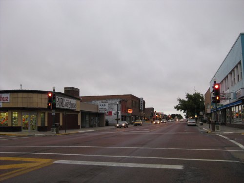 A quiet street scene with shops on either side, traffic lights, and overcast skies.