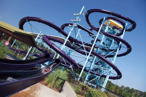 A colorful water slide with multiple twists and turns, set against a clear blue sky.